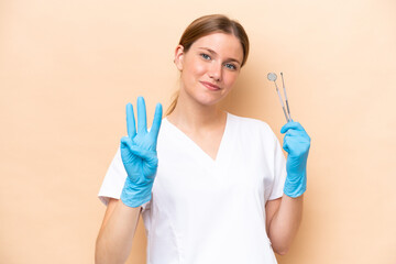 Dentist caucasian woman holding tools isolated on beige background happy and counting three with fingers