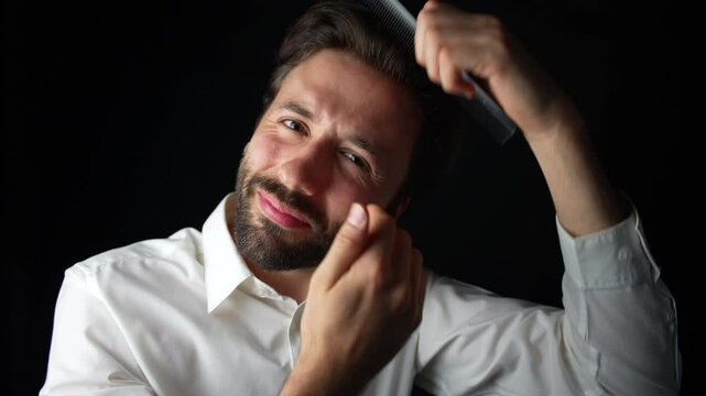 A young Caucasian man in a white shirt smiles at the camera while combing his hair