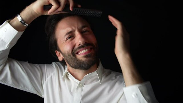 A young Caucasian man in a white shirt smiles at the camera while using a comb to adjust his hair