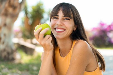 Young woman at outdoors holding an apple with happy expression