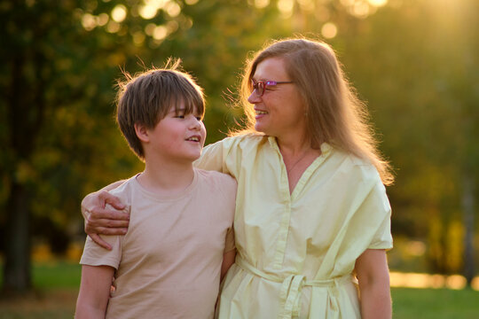The close relationship between the mother and her boy is evident as they laugh together under the sun. The joy of motherhood shines in the eyes of this woman as she embraces her teenage son in park.