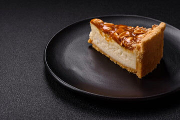 Delicious fresh cheesecake caramel peanut cake with cream and nuts on a ceramic plate on a dark concrete background