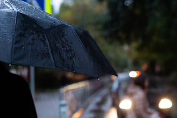 Portrait of a person holding black umbrella outside during the rain. Raindrops and light from city...