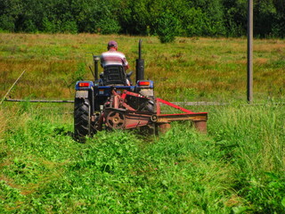 A farmer is mowing the grass with a rotary mower attached to a mini tractor