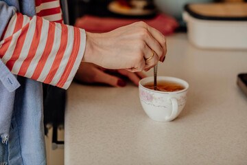 Morning Rituals, woman s hand, stirs a cup of tea in delicate white cup adorned with soft floral patterns in shades of pink