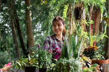 Young Asian woman in plaid shirt gardening outdoors. Smiling while arranging flowers in pots....