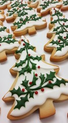 Obraz premium Christmas tree cookies decorated with white icing and green holly leaves, arranged on a light background. Shaped like Christmas trees, these cookies are festive and charming.
