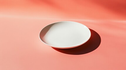 A white plate with a ribbed design sits on a pink surface against a peach-colored wall with shadows.