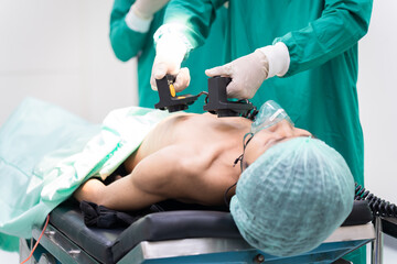 Asian surgical team in green scrubs using defibrillator on patient in operating room. Focus on emergency, professional teamwork ensuring patient safety effective response, and healthcare in hospital