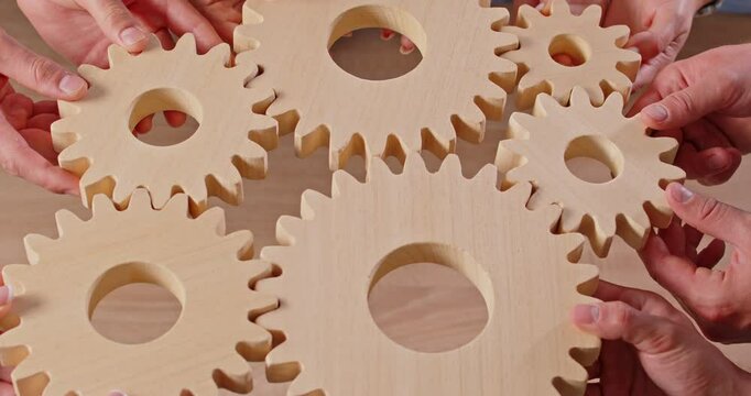 Close up of a business people team hands holding gears, symbolizing teamwork, collaboration, and the interworking parts of a successful group. Each cogwheel represents a crucial element in work.