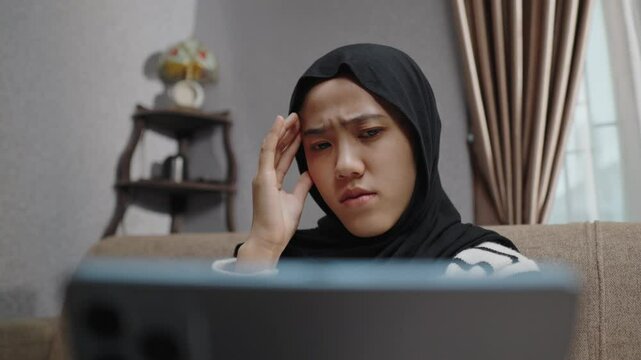 A muslim woman feeling anxious and stressed while reading bad news and negative comments on her gadget. Disappointed and frustrated facial expression due to the impact of social media on mental health