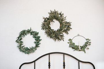 Decorative wreaths made of greenery hung on a white wall above a bed © reddish