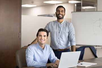 Obraz premium Two positive confident male managers posing for portrait in boardroom, using laptop for working together, meeting for partnership, professional discussion, corporate support