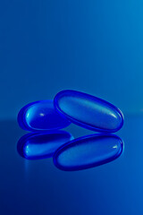 A close-up macro shot of two blue pills resting on a reflective surface.