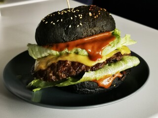 Black burger with beef patty, cheddar cheese, lettuce, and sauce on a plate