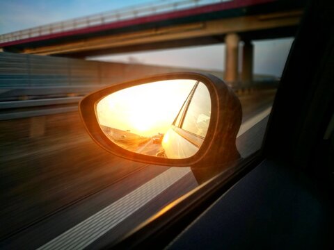 Sunset reflecting in car side mirror while driving on highway