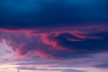 Ciemna, kłębiasta chmura oświetlona czerwonymi promieniami zachodzącego słońca. © boguslavus