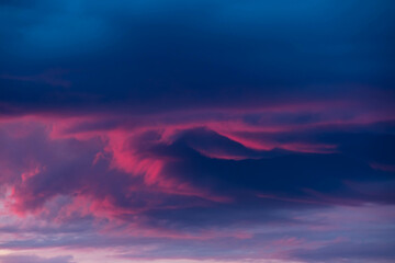Ciemna, kłębiasta chmura oświetlona czerwonymi promieniami zachodzącego słońca. © boguslavus