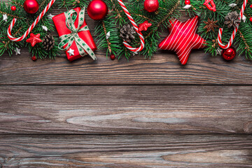 Christmas background with fir tree branches, gift boxes, red decorations, candy and pine cones on rustic wooden table. Flat lay. Happy New Year and winter holidays layout. Top view