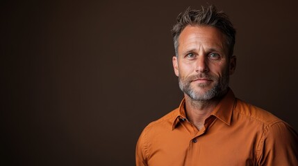 Fototapeta premium A mature man with a friendly expression and gray hair, wearing an orange shirt, portrayed against a neutral background, capturing a moment of warmth and approachability.