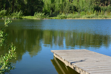 a wooden dock on the blue lake with green forest in the background