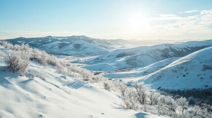 Fototapeta premium Snow-covered hills and mountains with a clear blue sky above and soft sunlight shining down