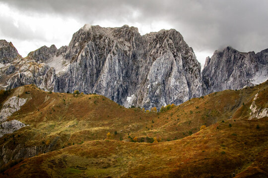 View of the rocky, sharp Karanfil peak and cloudy sky above the Grebaje Valley covered with yellow grass, Accursed Mountains in Montenegro (Prokletije, Albanian Alps), Three Peaks trail