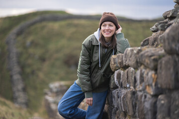 Woman tourist with Hadrian's wall on the background, happy Traveler travel Northumberland, United Kingdom. Destination and Vacation