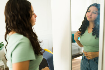 Latin teenage girl at home admiring herself in the mirror, gently caressing her hair and smiling