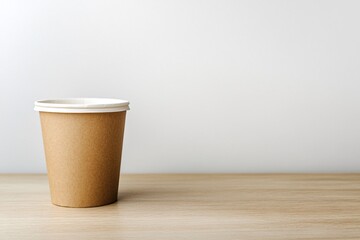 A plain brown takeaway coffee cup sits on a wooden table against a green backdrop in a well-lit cafe setting