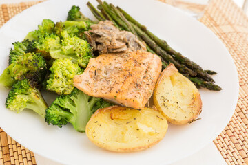 Delicious dish of fried river trout fillet with garnish of broccoli, asparagus sprouts, baked potatoes and mushroom sauce