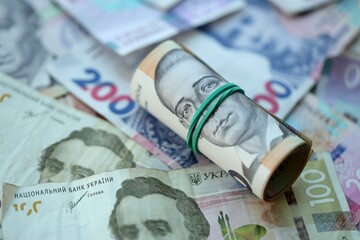 Roll of 500 Ukrainian Hryvnia money bills lies on big pile of ukrainian currency money close up