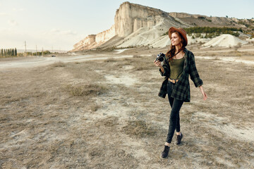 Woman in plaid shirt and hat takes photos in desert landscape with camera in hand