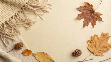 A beige knit blanket with frayed edges framing a neutral background with autumn leaves and pine cones