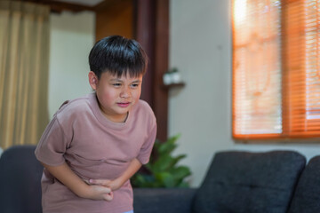 Portrait of sick unhappy little child asian boy touching belly stomach with suffering from stomach...