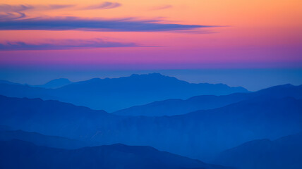 Fototapeta premium Stunning sunset over layered mountain ranges with vibrant hues of pink and purple across the sky in a serene landscape at dusk