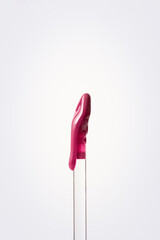 Vertical close-up shot of a purple lip gloss that flows down the wand on a clean white background....