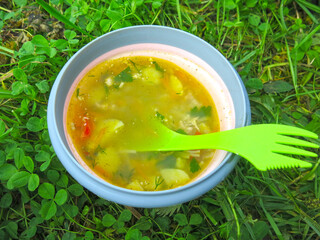 vegetable soup in a camping plate on the grass, on a spoon the inscription: Life is beautiful