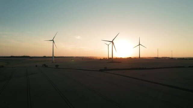 Wind turbines stand against an expansive field at sunset, framed by open farmland and warm atmospheric hues.