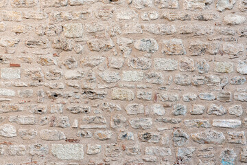 Rough stone wall with visible textures and uneven, weathered rocks, creating rustic and historic...