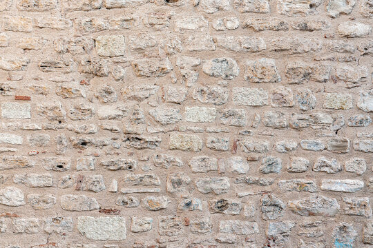 Rough stone wall with visible textures and uneven, weathered rocks, creating rustic and historic look. Ideal as natural background or architectural texture - Powered by Adobe