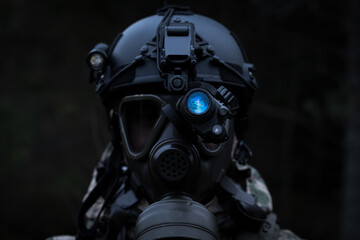 A soldier in a gas mask and a helmet with a night vision device in the forest at dusk.