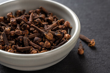 Whole cloves spice in a bowl over black background. Dry clove buds in a gray ceramic bowl macro. Cooking, herbal medicine and spice concept.