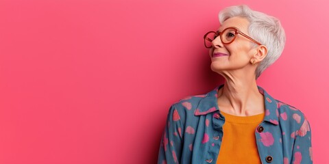 A woman in glasses and a blue jacket is smiling at the camera. The pink background adds a pop of color to the scene