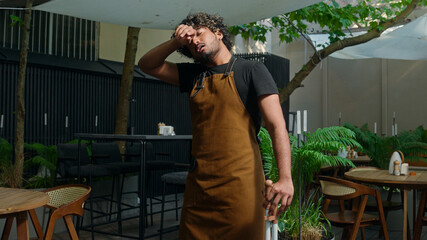 Tired exhausted Indian Arabian ethnic male man guy in apron waiter cleaner barista street food...