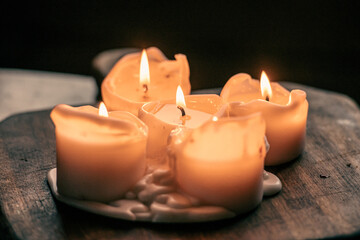 Wax candles burning on a wooden board or table, warm and dark background, close up