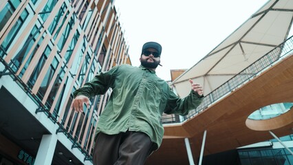 Low angle view of hipster pose in hip hop style surrounded by mall view. Portrait of sporty asian hip hop choreographer dancing break dance while looking at camera. Outdoor sport 2024. Hiphop.