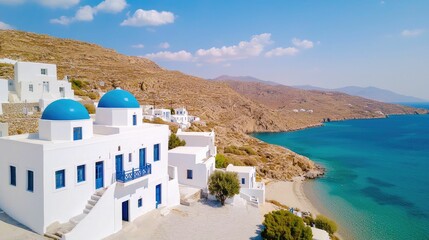 Obraz premium A scenic view of white buildings with blue domes along a coastal landscape, featuring crystal-clear waters and a mountainous backdrop.