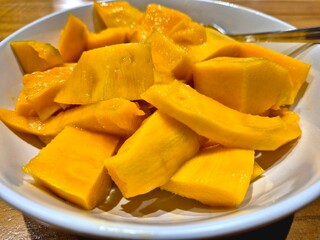 A bowl of sliced mangoes on a wooden table. Photo was taken close up. Selective focus.