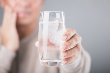 Man holding a glass of cold water with ice, showing a slight grimace due to tooth sensitivity....